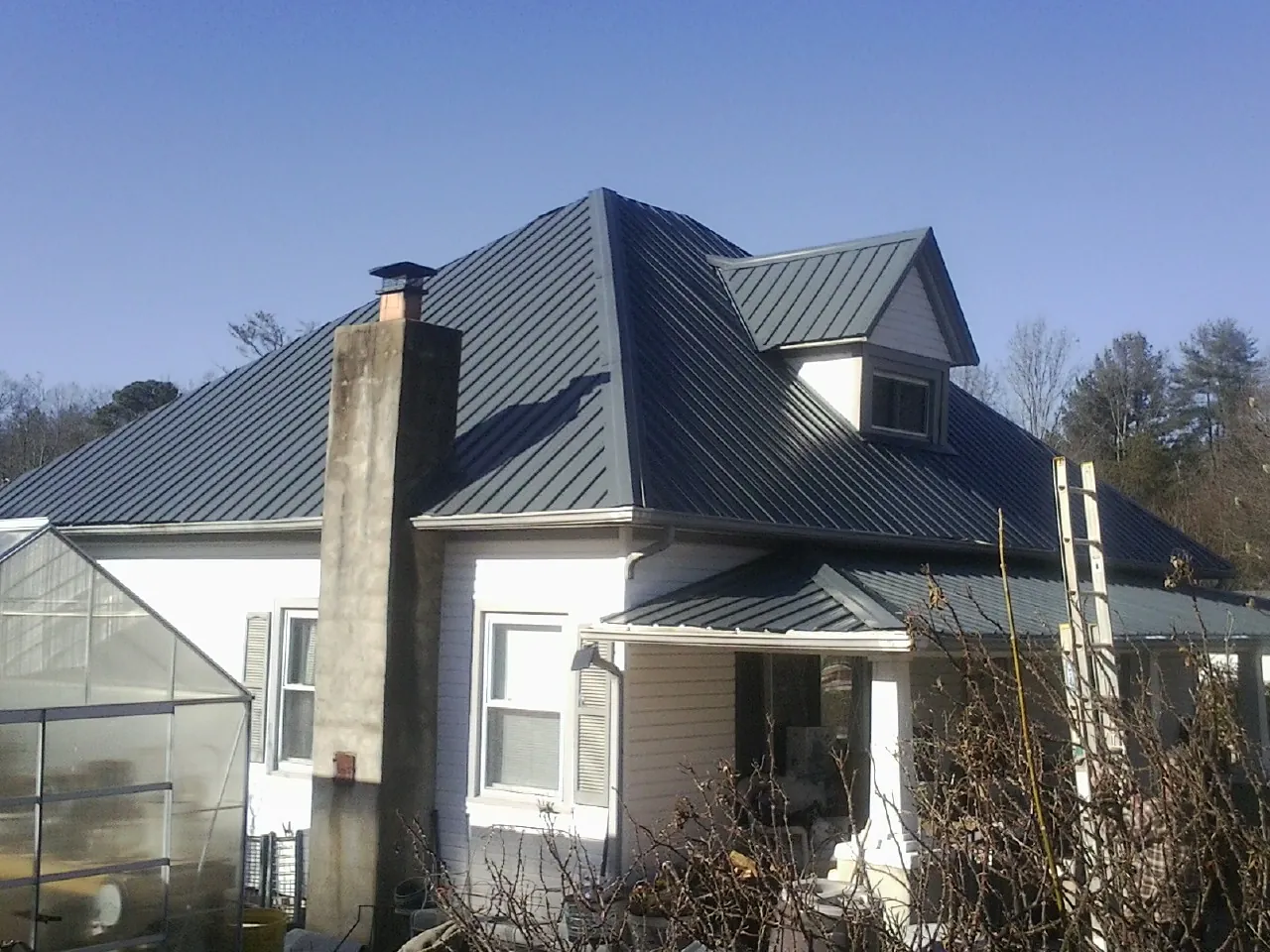Dark blue standing seam metal roof on a white farmhouse with dormer — Slate & Tile Roof Repair by Roofing Brothers in Atkins