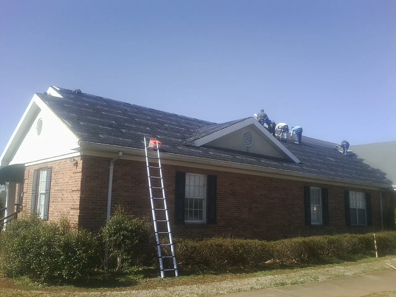 Crew tearing shingles off a brick ranch roof with a ladder set — Emergency Roof Repair work by our crew in Atkins