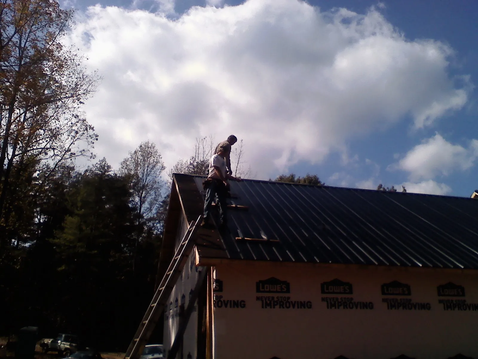 Roofer fastening dark metal panels high against a cloudy sky, from a Roof Inspection job in Atkins