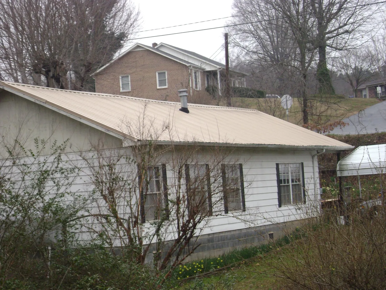 Tan metal roof on a white sided house set into a hillside — Commercial Roofing by Roofing Brothers in Atkins