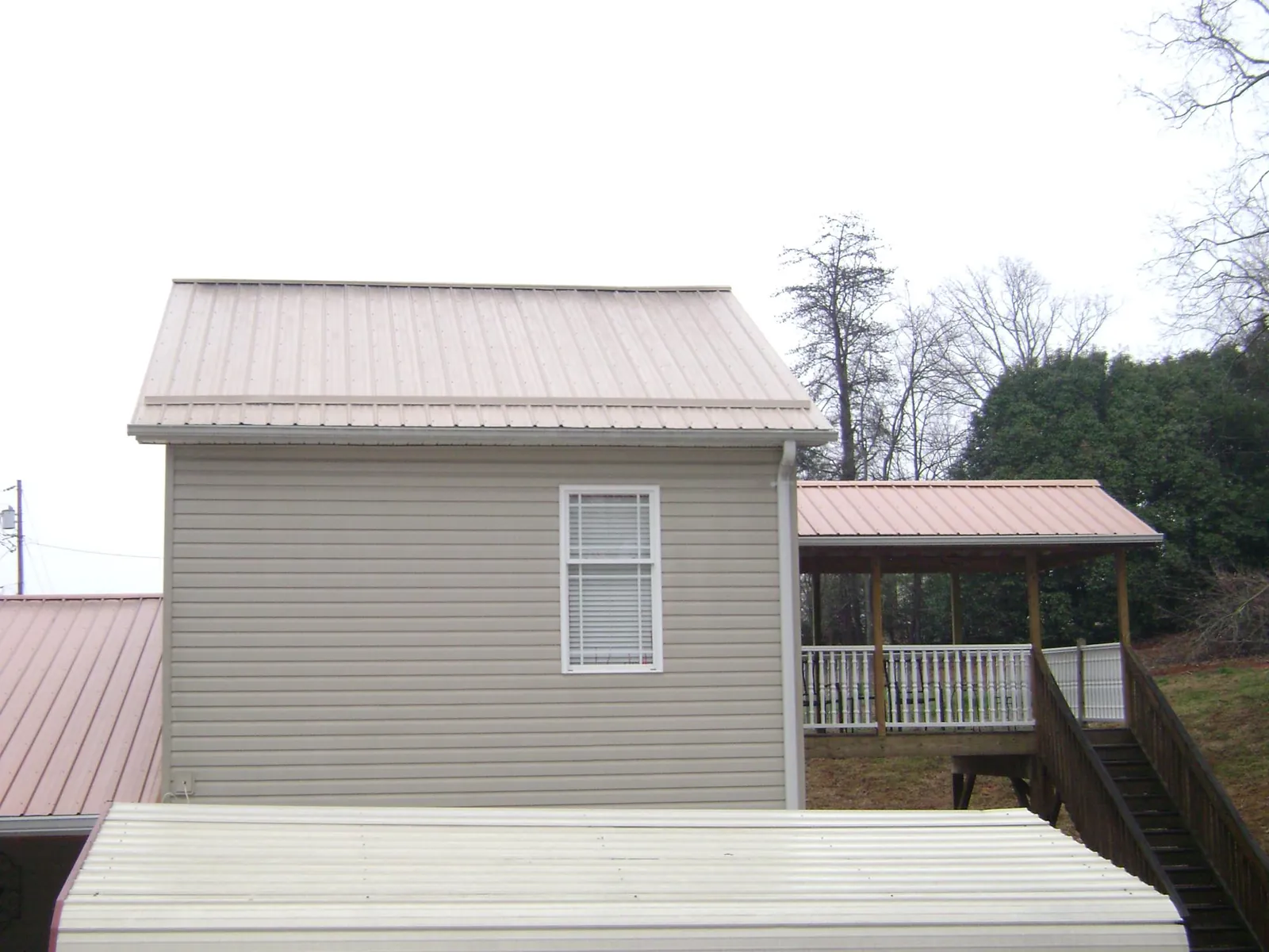 Tan metal roofs on a two story addition and attached porch, from a Roof Replacement job in Atkins